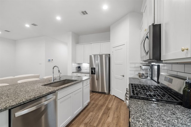 kitchen with white cabinetry, appliances with stainless steel finishes, decorative backsplash, dark stone counters, and sink