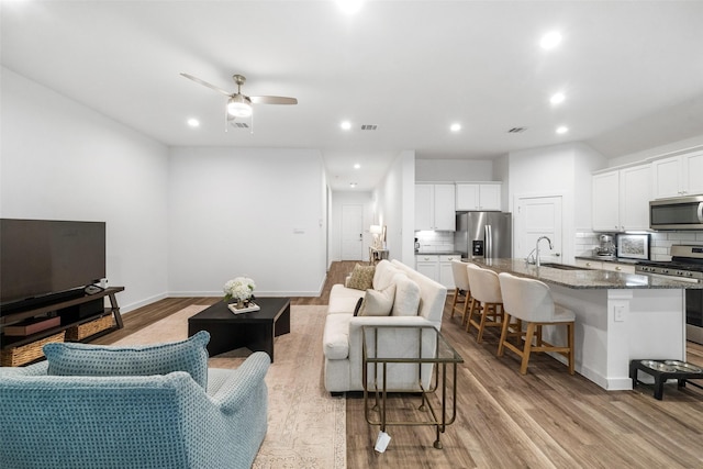 living room with light wood-type flooring, ceiling fan, and sink