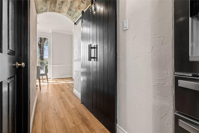 corridor featuring brick ceiling, light wood-type flooring, a barn door, ornamental molding, and lofted ceiling