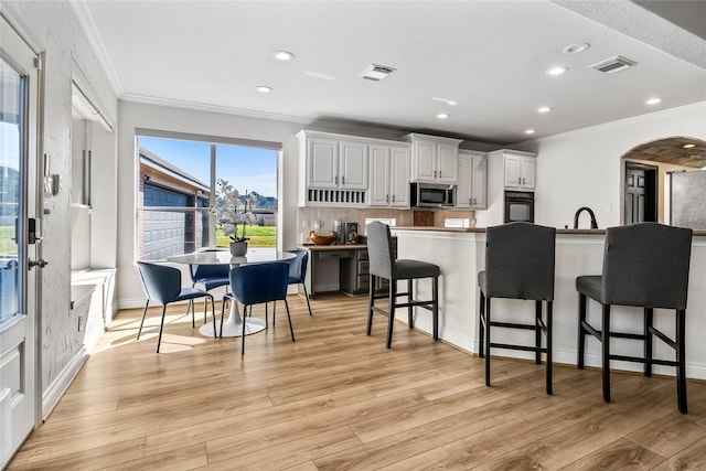 kitchen featuring white cabinets, light wood-type flooring, oven, and a kitchen bar