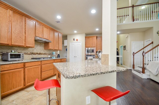 kitchen with appliances with stainless steel finishes, a kitchen bar, under cabinet range hood, decorative backsplash, and a toaster