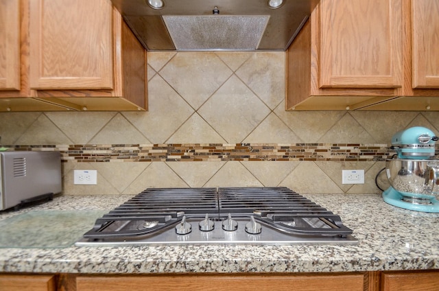 kitchen featuring light stone counters, ventilation hood, stainless steel gas stovetop, and tasteful backsplash