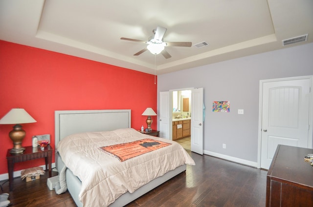 bedroom with dark hardwood / wood-style floors, ensuite bath, ceiling fan, and a raised ceiling