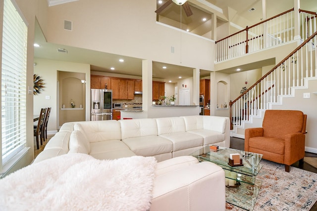 living area featuring a high ceiling, visible vents, baseboards, stairs, and ceiling fan