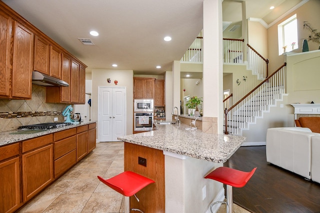 kitchen with under cabinet range hood, visible vents, a sink, a kitchen bar, and appliances with stainless steel finishes