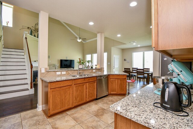 kitchen with light stone counters, stainless steel dishwasher, a sink, brown cabinetry, and ceiling fan