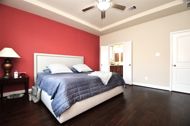 bedroom with a raised ceiling, wood finished floors, visible vents, and baseboards