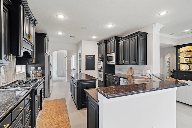 kitchen featuring kitchen peninsula, sink, a kitchen island, decorative columns, and stainless steel appliances