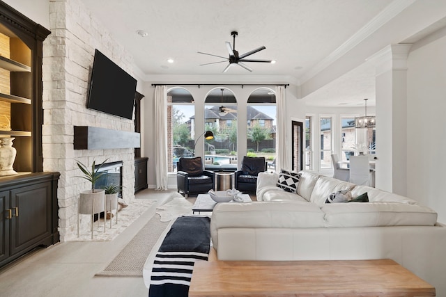 living room with crown molding, ceiling fan with notable chandelier, and a stone fireplace