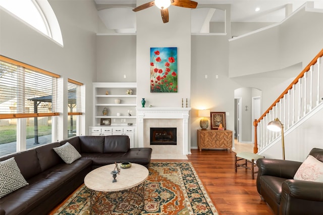 living room with a high ceiling, a tile fireplace, hardwood / wood-style floors, and ceiling fan