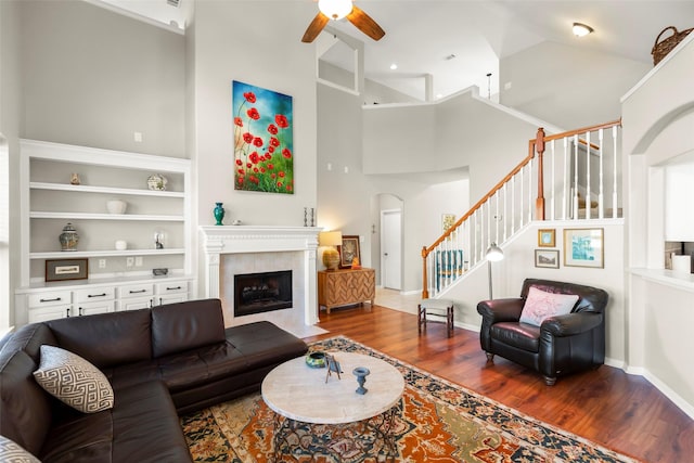 living room with built in features, ceiling fan, hardwood / wood-style floors, high vaulted ceiling, and a tiled fireplace