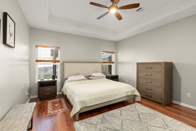 bedroom with dark hardwood / wood-style flooring, a tray ceiling, and ceiling fan