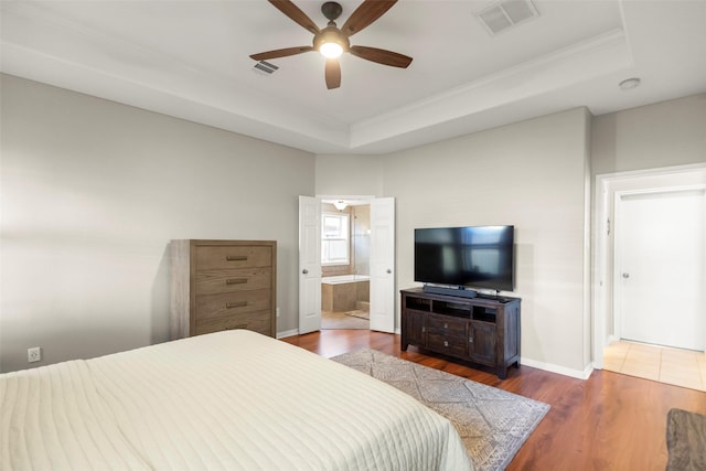 bedroom featuring dark hardwood / wood-style flooring, ensuite bath, a raised ceiling, and ceiling fan