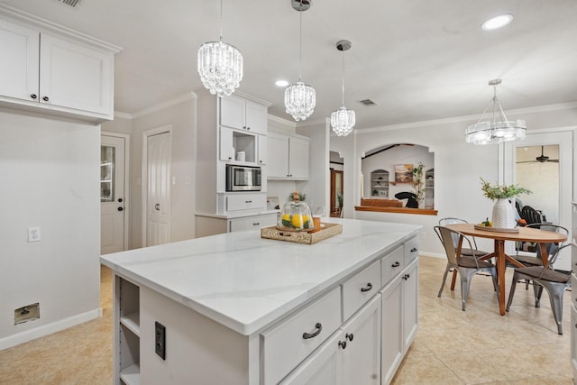 kitchen featuring stainless steel microwave, light stone counters, white cabinets, and hanging light fixtures