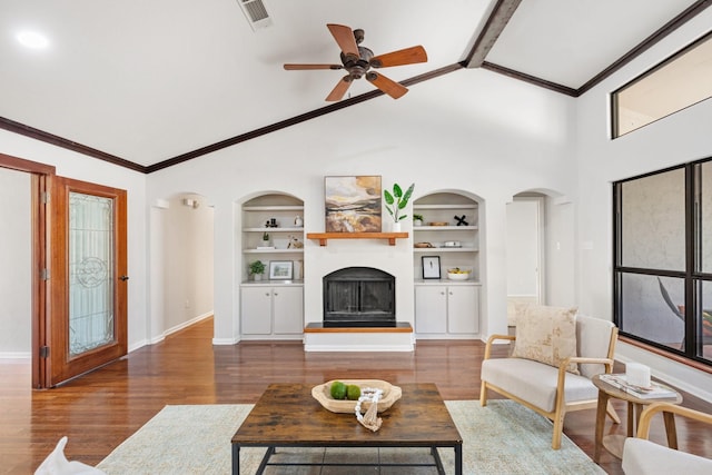 living area with a fireplace with raised hearth, lofted ceiling with beams, built in shelves, wood finished floors, and visible vents