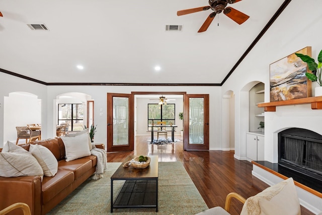 living room featuring a fireplace with raised hearth, built in shelves, visible vents, and crown molding