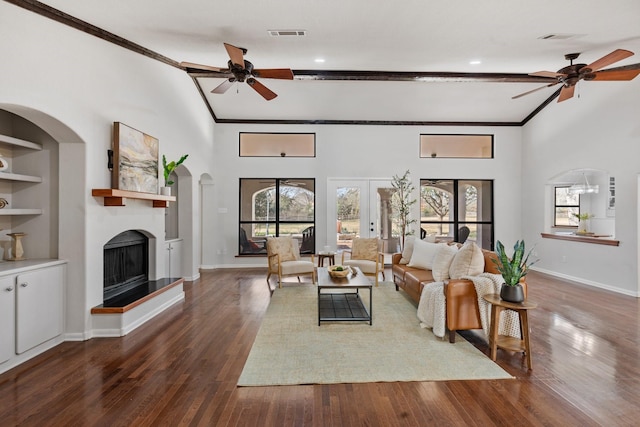 living room with built in features, a fireplace with raised hearth, crown molding, and wood finished floors