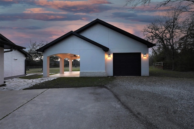 property exterior at dusk with a garage, gravel driveway, and stucco siding