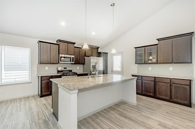 kitchen featuring lofted ceiling, pendant lighting, dark brown cabinetry, light stone countertops, and stainless steel appliances