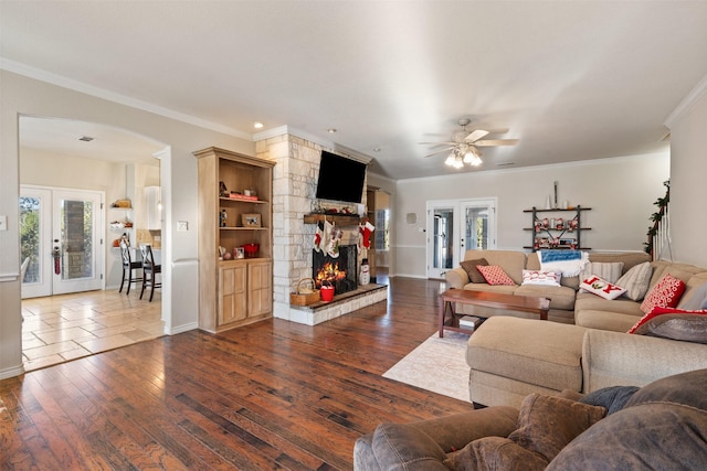 living room with a stone fireplace, french doors, dark hardwood / wood-style floors, ceiling fan, and crown molding