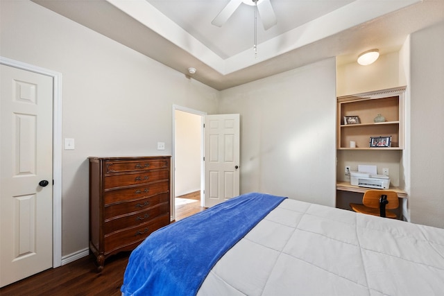 bedroom with ceiling fan, dark hardwood / wood-style floors, a tray ceiling, and built in desk