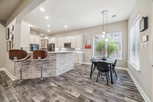 kitchen featuring white cabinetry, hanging light fixtures, appliances with stainless steel finishes, dark hardwood / wood-style flooring, and decorative backsplash