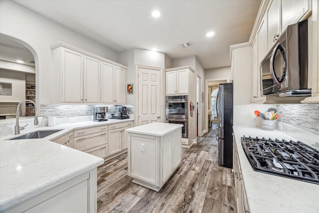 kitchen featuring sink, stainless steel appliances, light stone counters, white cabinets, and a kitchen island