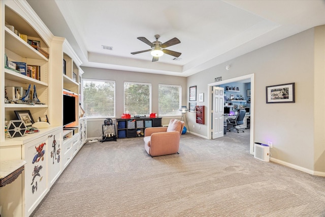 living area featuring a raised ceiling, light carpet, and ceiling fan