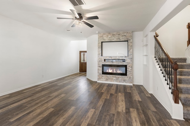 unfurnished living room featuring ceiling fan, dark wood-type flooring, and a stone fireplace