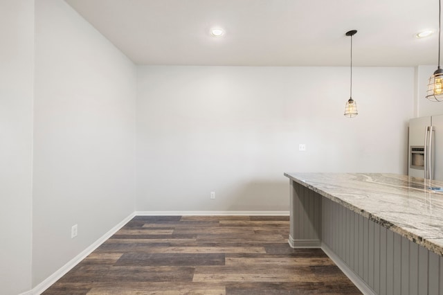 interior space featuring dark hardwood / wood-style flooring, pendant lighting, stainless steel fridge, and light stone counters