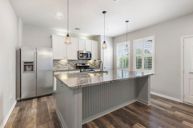 kitchen with white cabinetry, a center island with sink, stainless steel appliances, stone counters, and pendant lighting