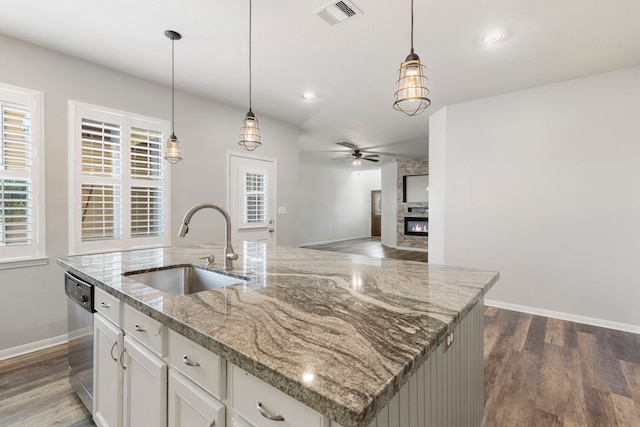 kitchen featuring a center island with sink, stainless steel dishwasher, sink, hanging light fixtures, and white cabinets