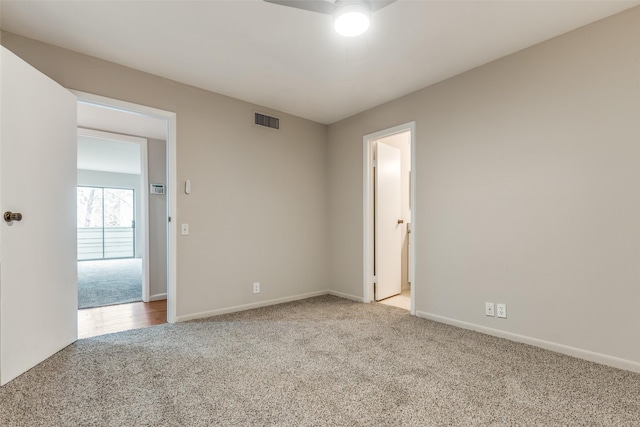 carpeted spare room featuring ceiling fan, visible vents, and baseboards