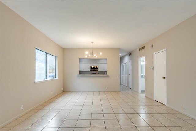 empty room featuring baseboards, light tile patterned flooring, visible vents, and a notable chandelier