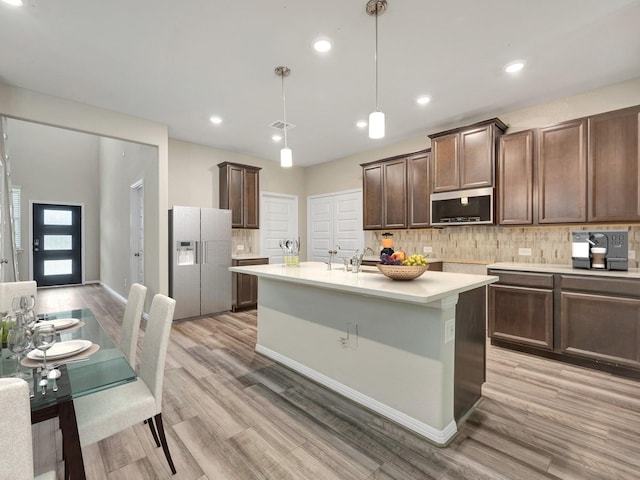 kitchen with a kitchen island with sink, light wood-type flooring, decorative light fixtures, white refrigerator with ice dispenser, and dark brown cabinetry