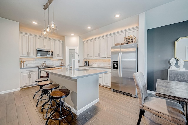 kitchen with appliances with stainless steel finishes, white cabinetry, sink, pendant lighting, and an island with sink