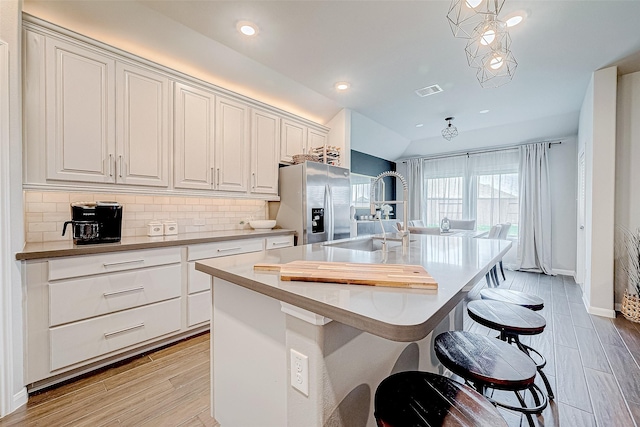 kitchen featuring a center island with sink, backsplash, pendant lighting, and stainless steel fridge with ice dispenser