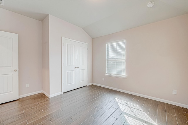 unfurnished bedroom with light wood-type flooring, a closet, and vaulted ceiling