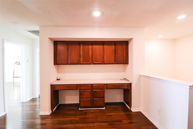 unfurnished office with a textured ceiling, dark hardwood / wood-style floors, and built in desk