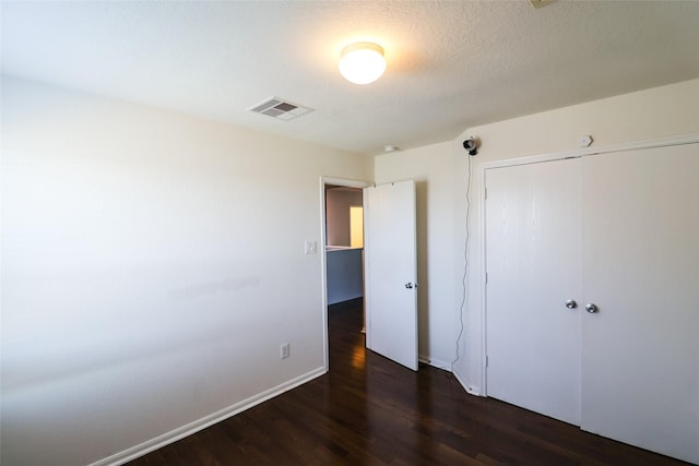 unfurnished bedroom featuring a textured ceiling, a closet, and dark hardwood / wood-style flooring