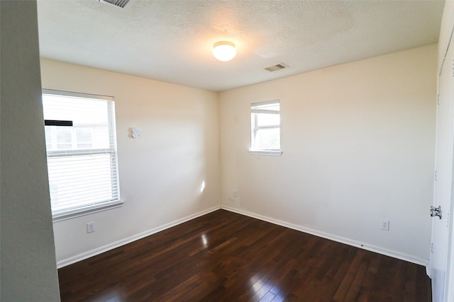 empty room with a textured ceiling, a healthy amount of sunlight, and dark hardwood / wood-style floors