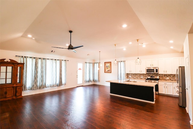 kitchen with lofted ceiling, stainless steel appliances, decorative backsplash, hanging light fixtures, and a center island with sink