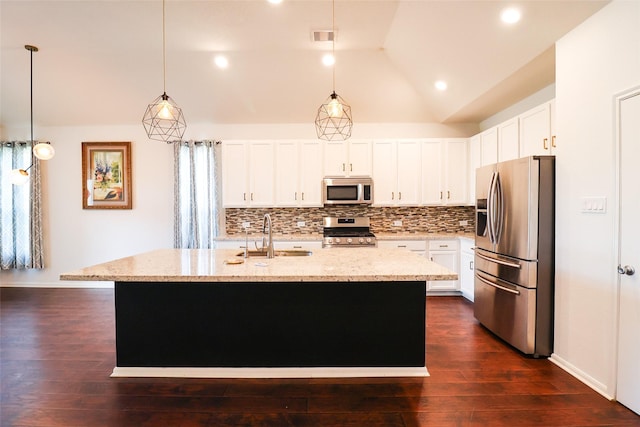 kitchen featuring appliances with stainless steel finishes, lofted ceiling, an island with sink, sink, and light stone counters