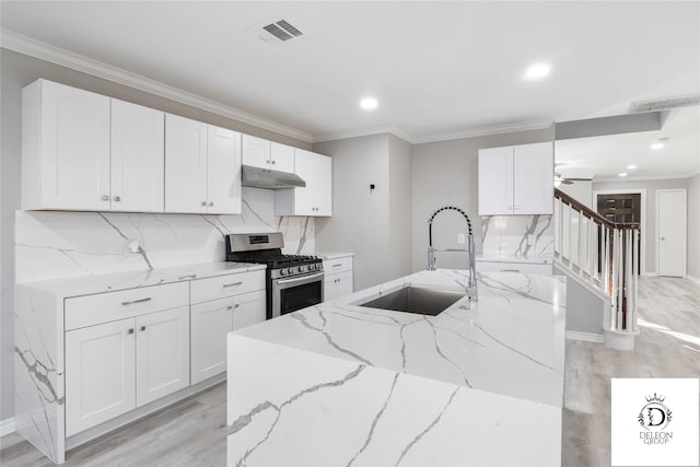 kitchen with gas stove, sink, white cabinetry, light wood-type flooring, and light stone countertops