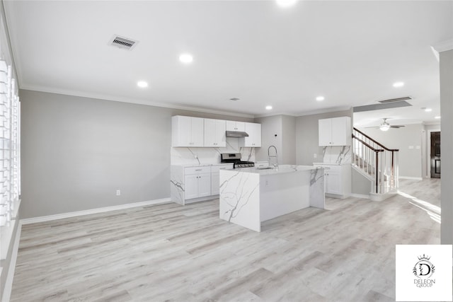 kitchen featuring a center island with sink, stainless steel range, light wood-type flooring, light stone countertops, and white cabinets