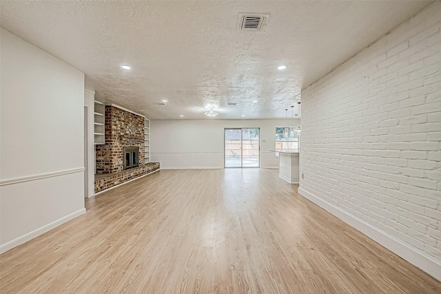 unfurnished living room with a textured ceiling, brick wall, a fireplace, and light hardwood / wood-style flooring