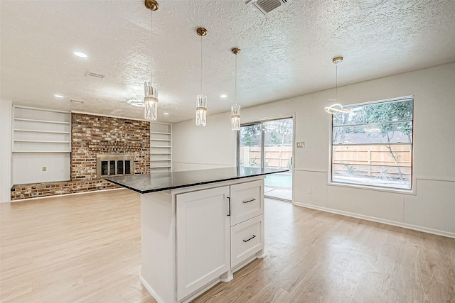 kitchen with white cabinetry, a brick fireplace, built in features, hanging light fixtures, and a textured ceiling