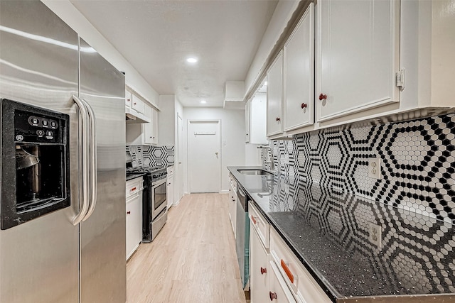 kitchen with tasteful backsplash, light hardwood / wood-style flooring, appliances with stainless steel finishes, white cabinets, and dark stone counters