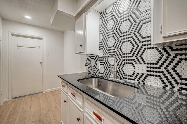 kitchen with a textured ceiling, white cabinetry, dark stone counters, sink, and light wood-type flooring