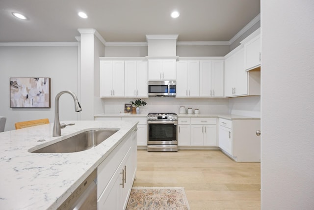 kitchen featuring white cabinetry, appliances with stainless steel finishes, light stone countertops, ornamental molding, and sink